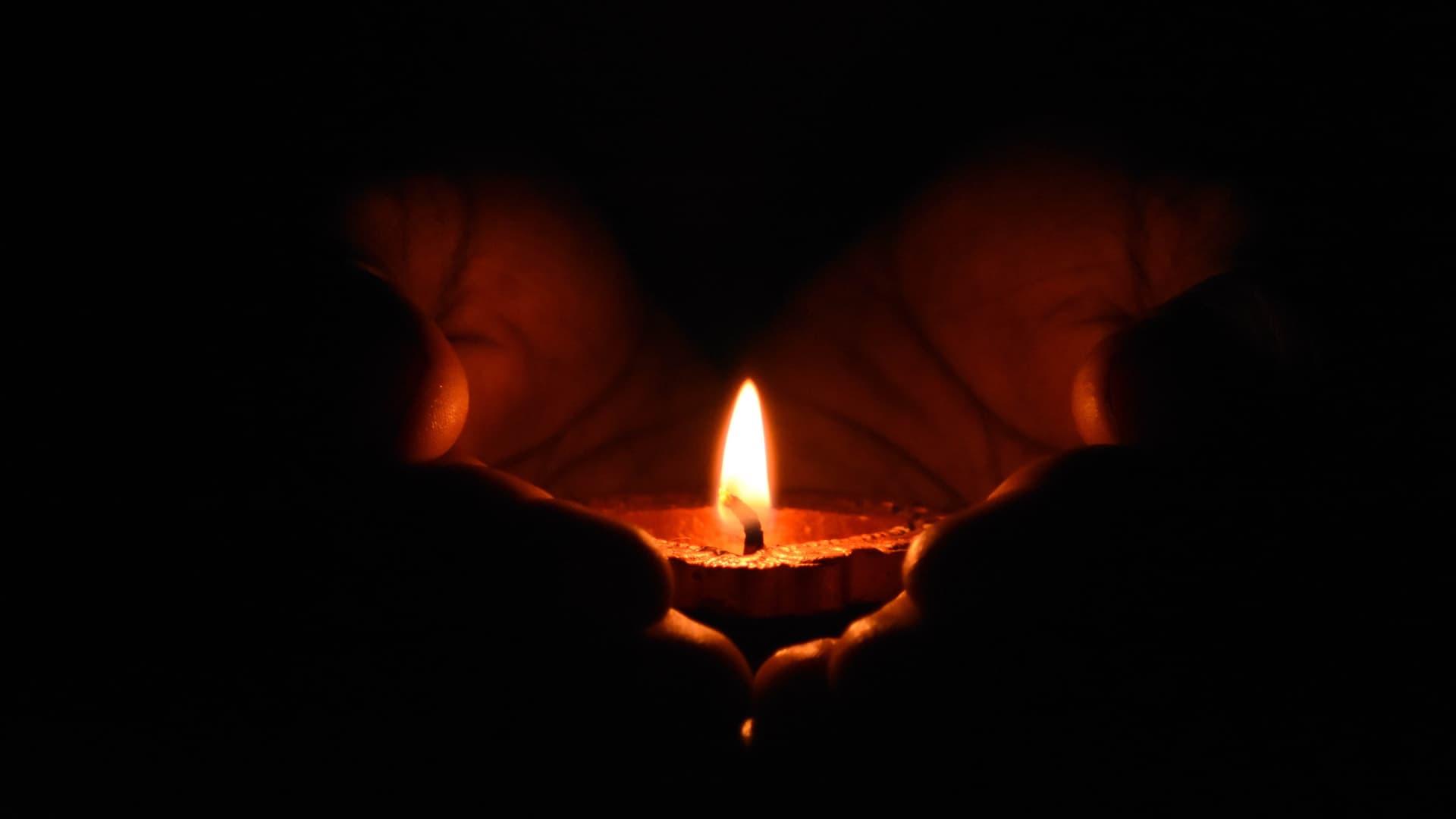 Hands tend to a small oil lamp flame