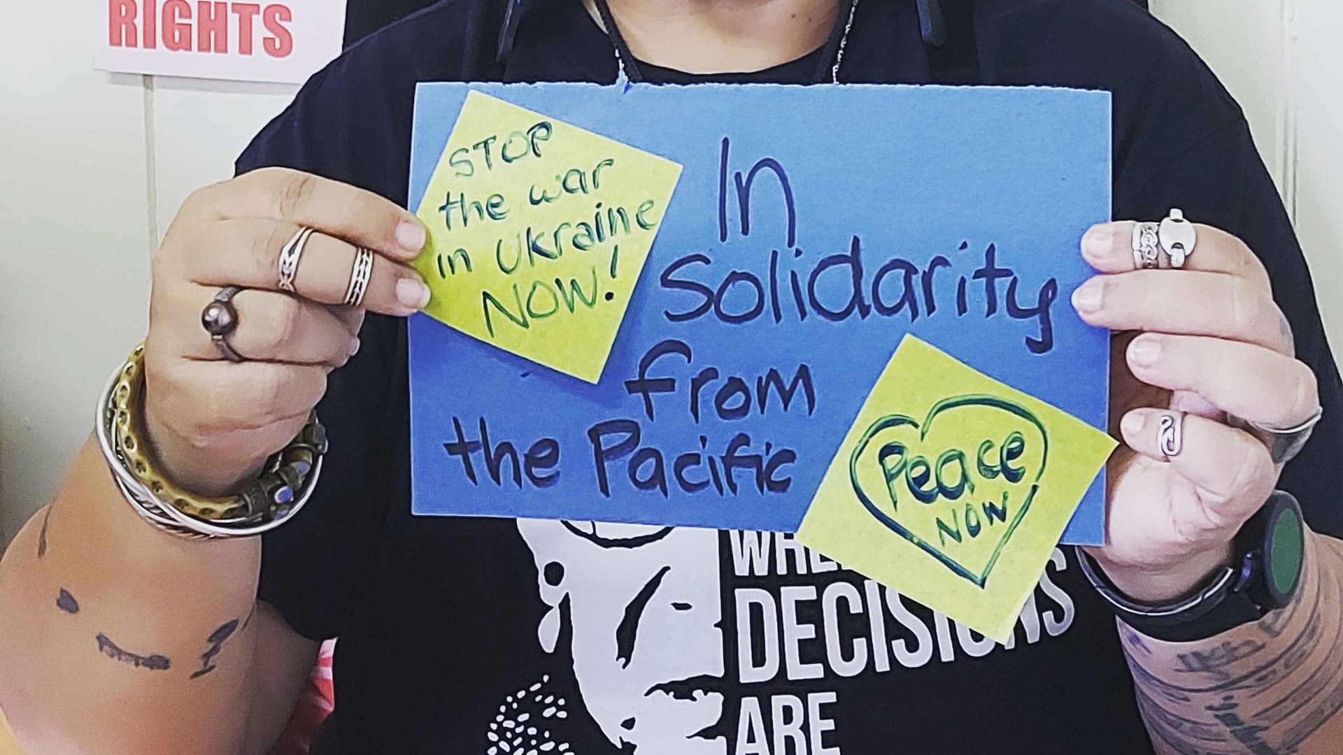 Simple poster sign held up. The sign reads stop the war. In solidarity for peace. Peace Now